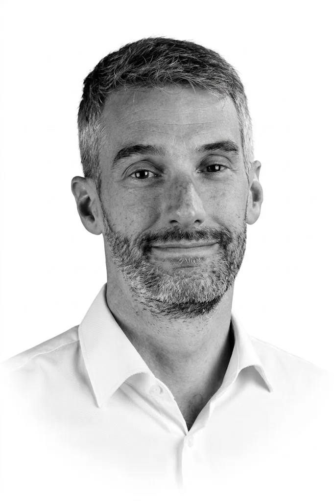 Black and white portrait of Etienne 'E.T.' Maujean, smiling, in a white shirt